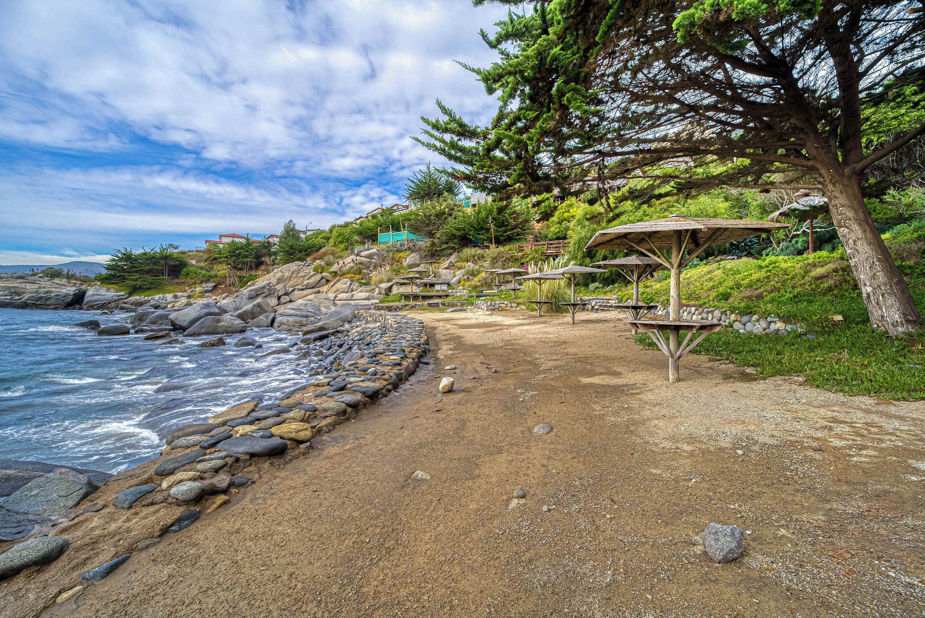 A rocky beach with a wooden gazebo and a stone wall.