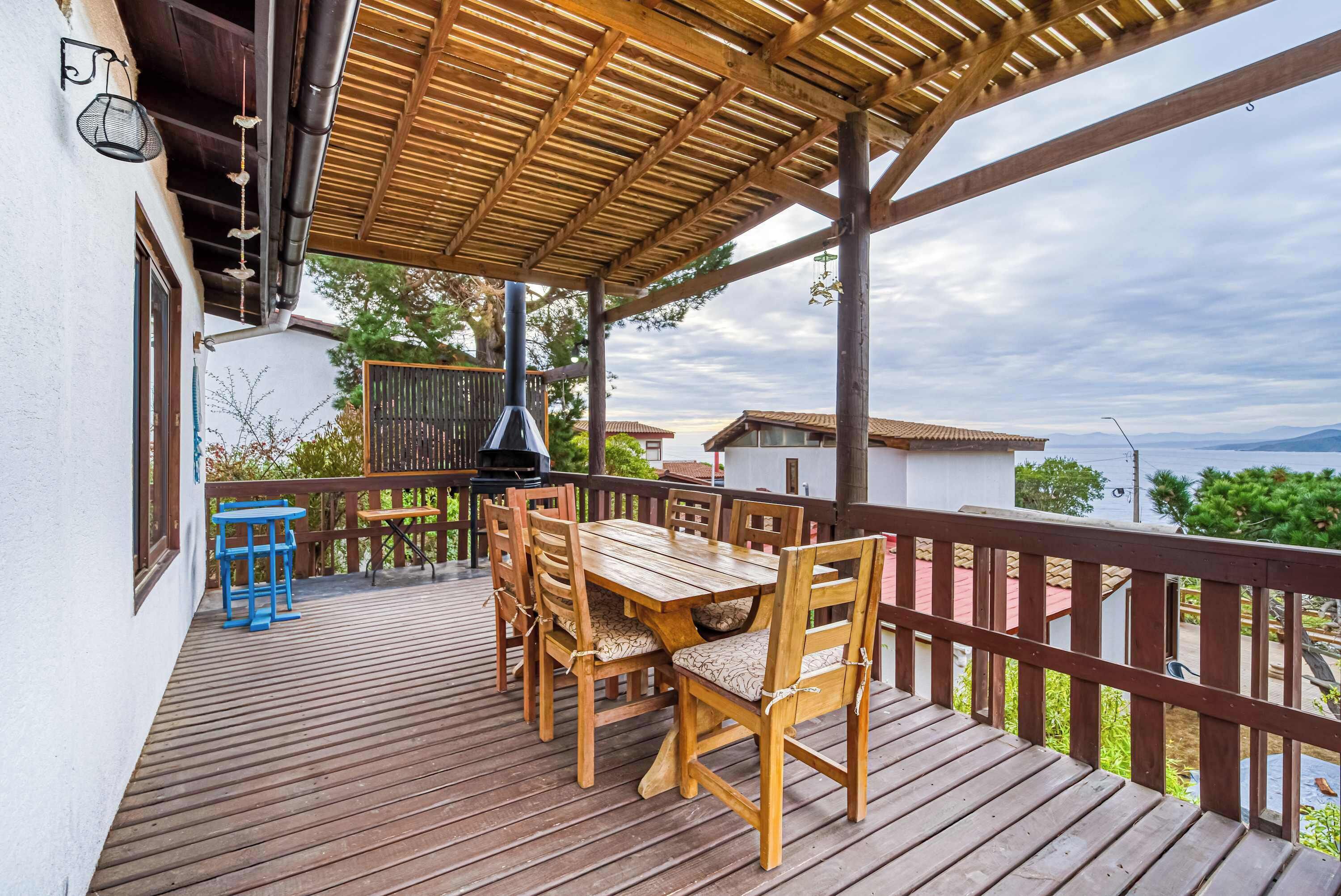 Een houten terras met een tafel, stoelen, een pergola en uitzicht op het omliggende landschap.