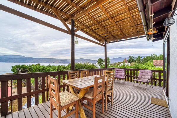 Una terraza de madera con una mesa y sillas, con vista panorámica a montañas y una masa de agua.