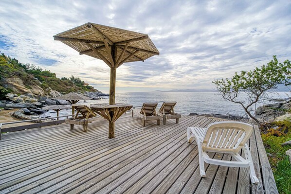 A wooden deck with a table and chairs, a parasol, and a view of the sea.