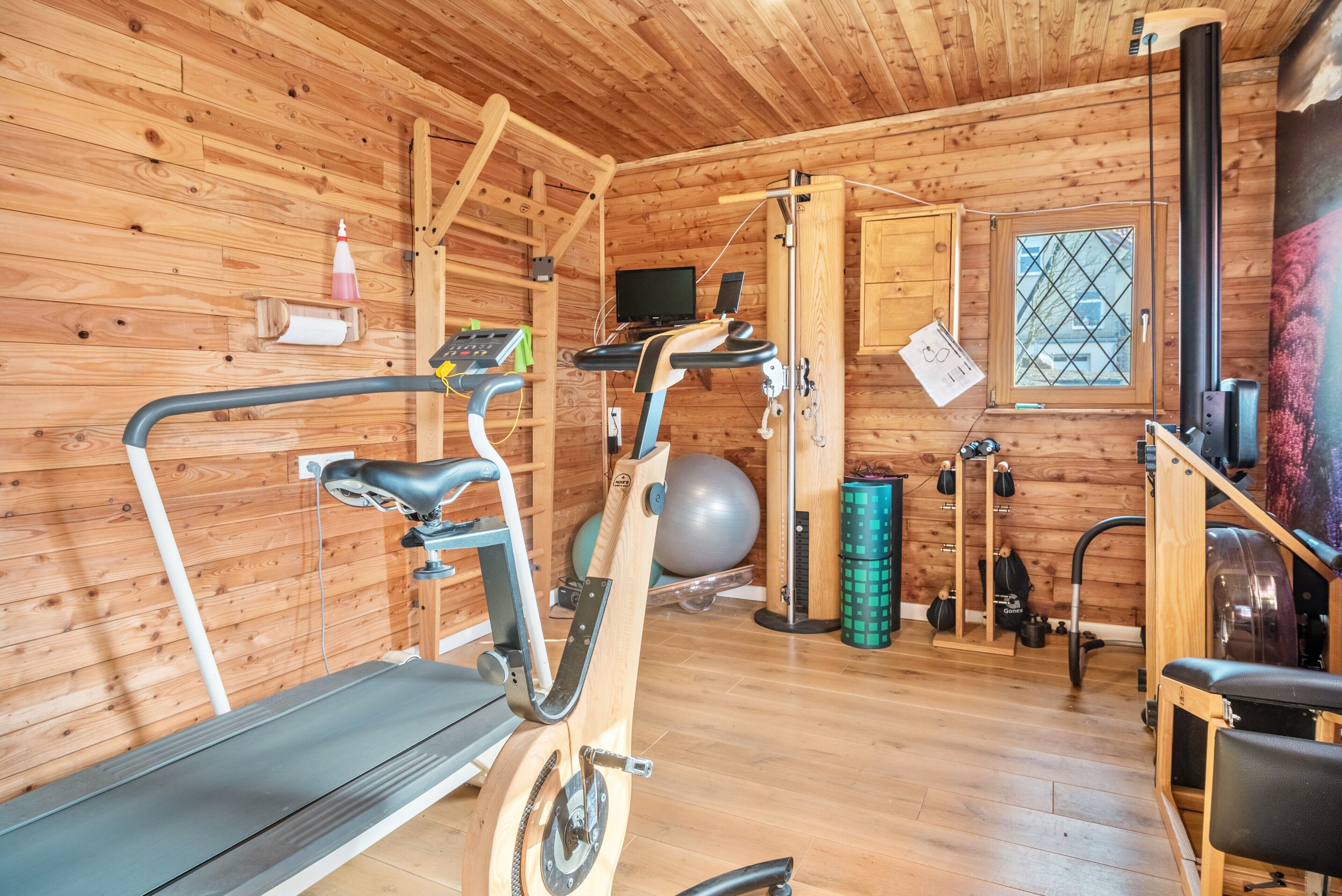 A wooden cabin with a treadmill, exercise ball, and weights.