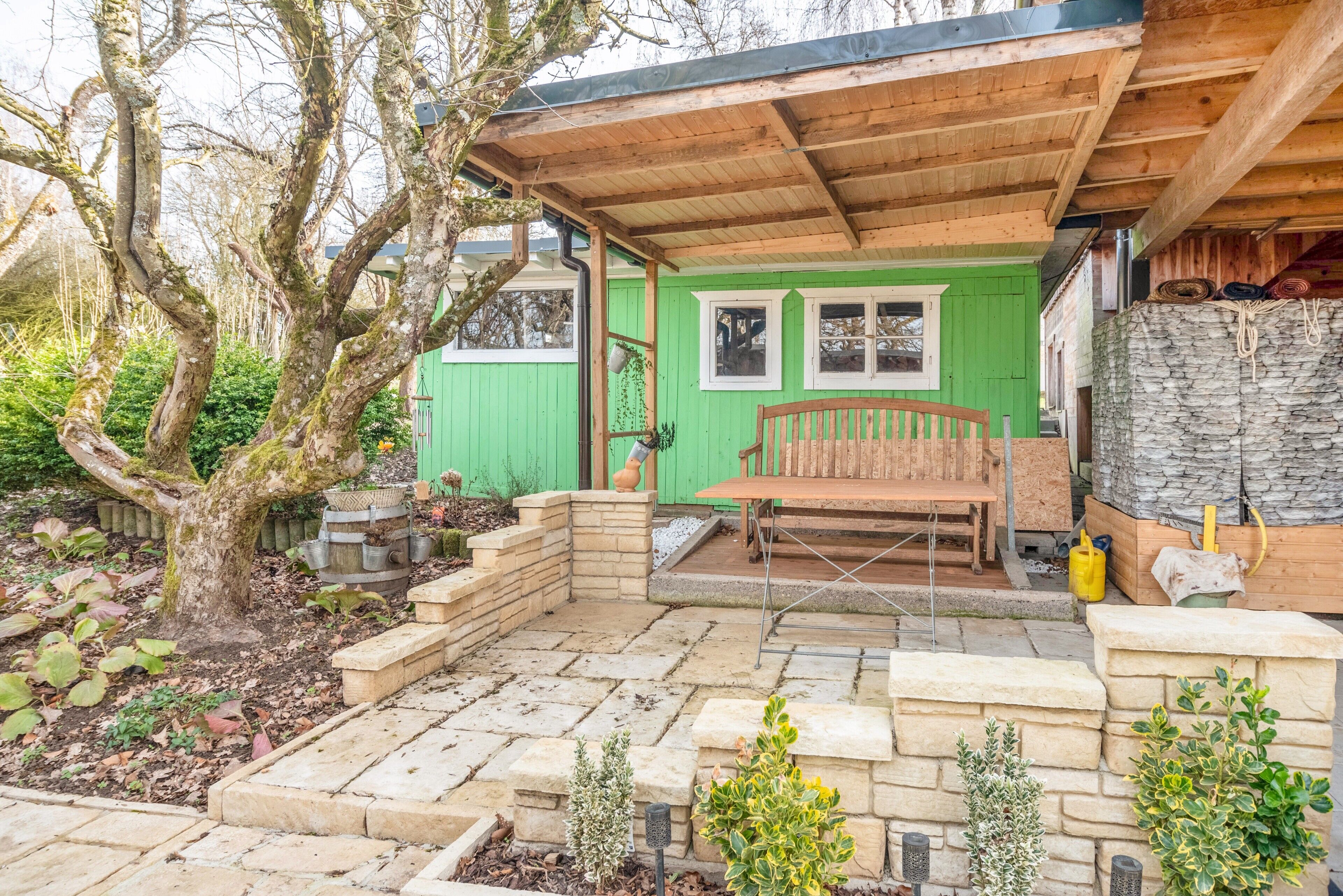 A wooden deck with a bench, a stone pathway, and a green building with windows.
