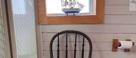 A wooden chair with a curved backrest and a dark finish, positioned in front of a window with a ship decoration.