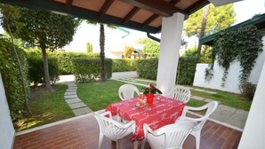 A covered patio with a table set for four, surrounded by white chairs, under a wooden roof structure. - Cozy Apartment With Shared Pool (San Michele al Tagliamento)