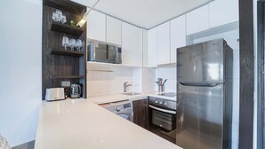 Een moderne keuken met witte kasten, een roestvrijstalen koelkast, een magnetron, een broodrooster en een wasmachine.