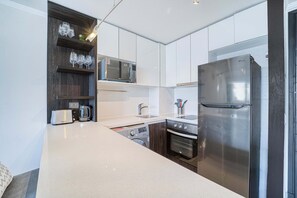 A modern kitchen with white cabinetry, a stainless steel refrigerator, a microwave, a toaster, and a washing machine. - Luz de Kennedy - 1D, Wifi, Mall & Parking (Las Condes)