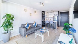 Een moderne woonkamer met een grijze bank, een glazen salontafel en een eethoek met een bar.