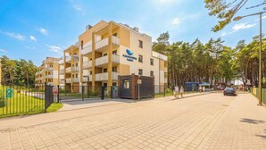 Un edificio de varios pisos con balcones, una entrada protegida por un portón y un cielo despejado.