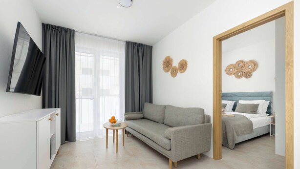 Una habitación de hotel moderna con sofá, cama, una mesita y televisión fijada en la pared.