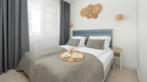 Una cama bien hecha con colcha gris, una mesita de noche con lámpara, y una obra de arte en la pared sobre la cama.