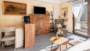 Un salon moderne avec un meuble en bois, un téléviseur à écran plat, un coin repas avec une chaise, un canapé et une vue à travers une porte vitrée.