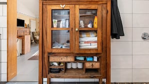 Un meuble en bois doté de portes en verre, contenant des articles de toilette et des serviettes.