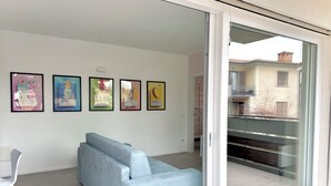 Ein modernes Wohnzimmer mit einem hellblauen Sofa, einem weißen Sessel und einer Glastür, die auf einen Balkon führt.