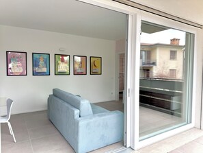 Ein modernes Wohnzimmer mit einem hellblauen Sofa, einem weißen Sessel und einer Glastür, die auf einen Balkon führt.