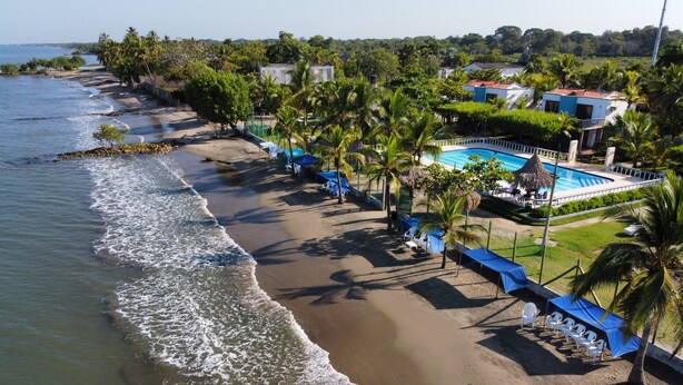 A beach with a swimming pool, palm trees, and a view of the ocean. - Ancla del galeon 7 (Tolú)