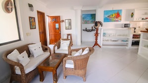 A living room with wicker furniture, a wooden door, a painting, and a white tiled floor. - Ancla del galeon 7 (Tolú)