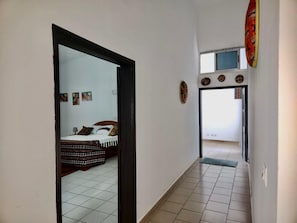 Passadís estret amb un llit a l'habitació esquerra, sòl de rajola i una porta que dona a una altra estança.