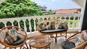 A balcony with wicker furniture, including chairs and a table, and a view of greenery and buildings in the background. - Private rooms in a Villa - Abidjan, Ivory Coast (Abidjan)