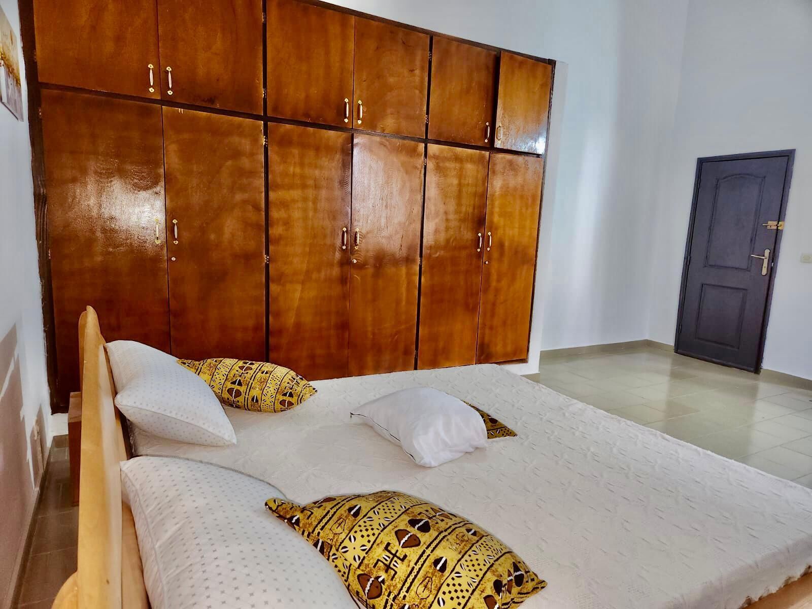 A bedroom with a wooden wardrobe, a bed with patterned pillows, and a plain door.