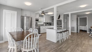 Una cocina moderna con muebles blancos, electrodomésticos de acero inoxidable y una isla central con taburetes de bar.