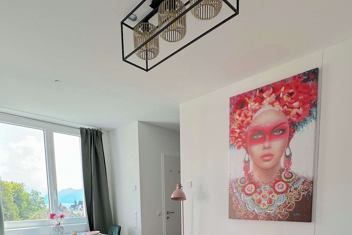 A modern living room with a glass coffee table, a pink sofa, a painting on the wall, and a view through the window.