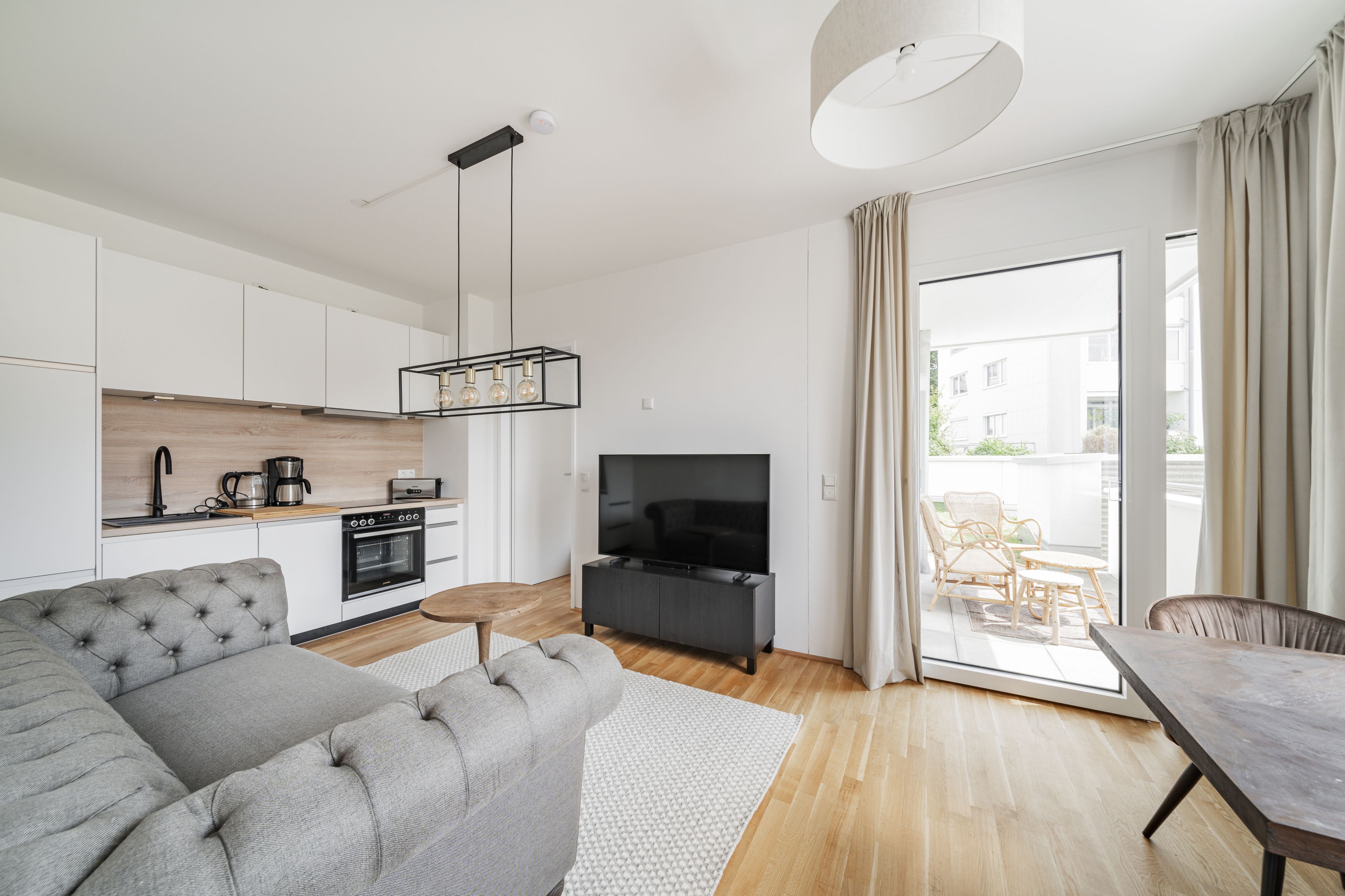 Ein modernes Wohnzimmer mit einem grauen Sofa, einem Fernseher und einem Essbereich mit Tisch und Stühlen.