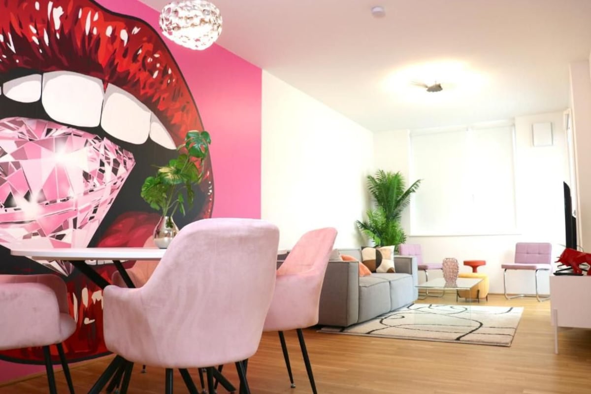 A modern living room with a pink wall, a large diamond artwork, and a grey sofa.