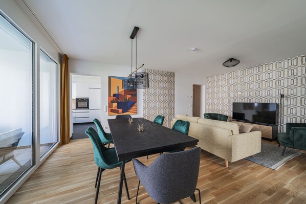 Een moderne woonkamer met een eettafel, bank, televisie en een keuken op de achtergrond.