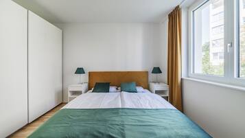 Un dormitorio con una cama, dos mesitas de noche con lámparas, una ventana con cortinas y un armario.