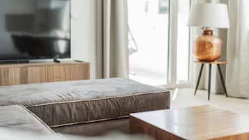 A modern living room with a flat-screen TV on a wooden cabinet, a grey sofa, a wooden coffee table, and a lamp on a small stand.