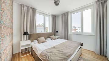 A modern bedroom with a large bed, two bedside tables, a nightstand, a ceiling light, and a view of the outside.
