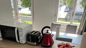 A kitchen with a microwave, toaster, kettle, and a bowl of tomatoes on the counter. There are pots and utensils in the drawer below. - Hanna Apartment Interlaken (Matten bei Interlaken)