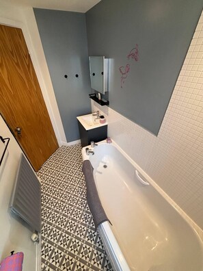 Ett badrum med badkar, handfat, spegel och ett mönstrat golv.