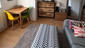 Ett rum med ett skrivbord i trä, två stolar, en soffa, en mönstrad pall, en spegel och en byrå med lådor.