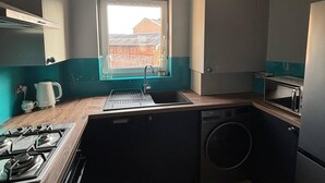 Ett kompakt kök med en gasspis, ett handfat, en tvättmaskin och ett fönster med utsikt över en byggnad utanför.