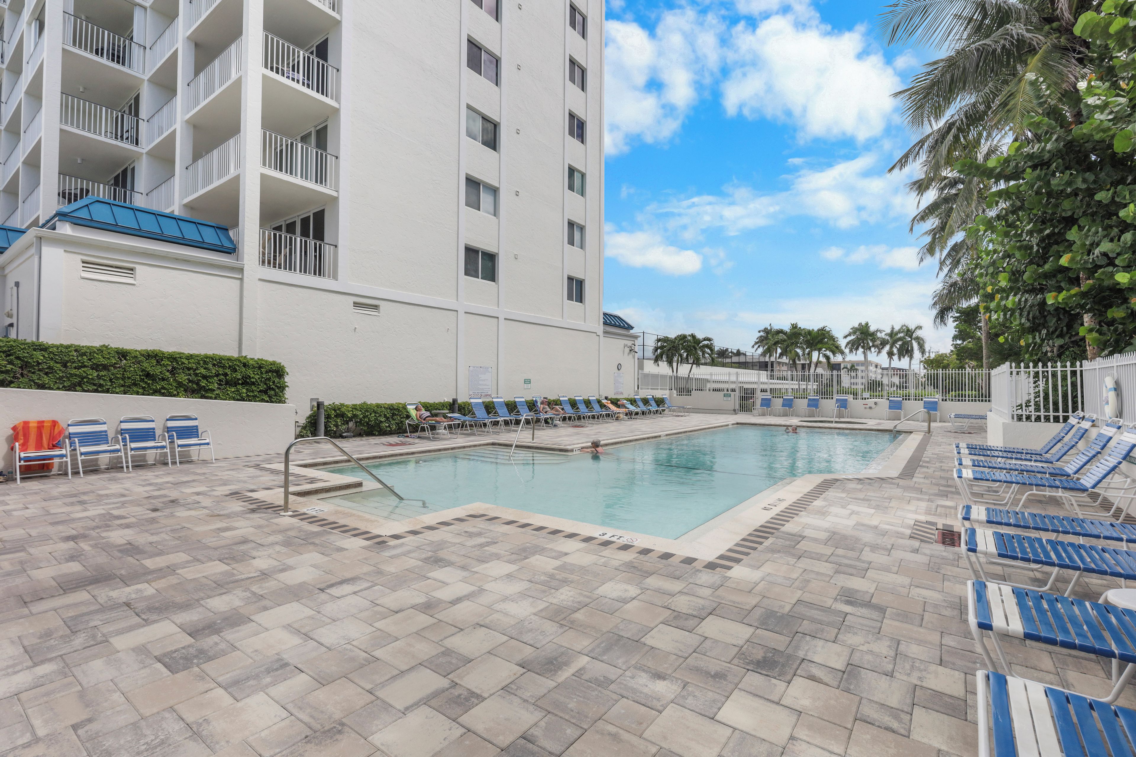 A pool area with lounge chairs and a building with multiple balconies.