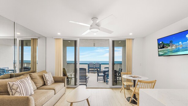 Un salon moderne comprenant un canapé, une table basse et un coin repas, donnant sur un balcon avec vue sur l’océan.