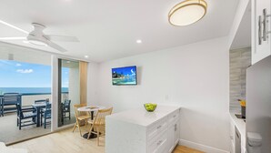 Une cuisine moderne avec un plan de travail en marbre blanc, un ventilateur de plafond et une vue sur l’océan, accessible par une porte-fenêtre coulissante.