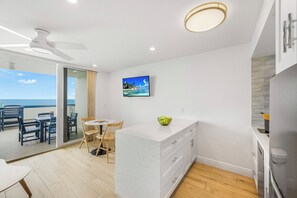 A modern kitchen with a white marble countertop, a ceiling fan, and a view of the ocean through a sliding glass door. - Coastal Beachfront Apollo Unit | Extended Balcony (Marco Island)