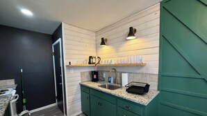 Eine moderne Küche mit grünen Schränken, einer Granitabdeckung und einer eingebauten Spüle. Über der Arbeitsplatte befinden sich Regale mit Gläsern und einer Kaffeemaschine.