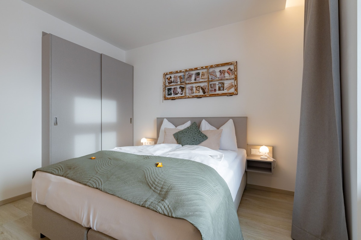 A bedroom with a bed, bedside lamps, a wall art piece, and a wardrobe.