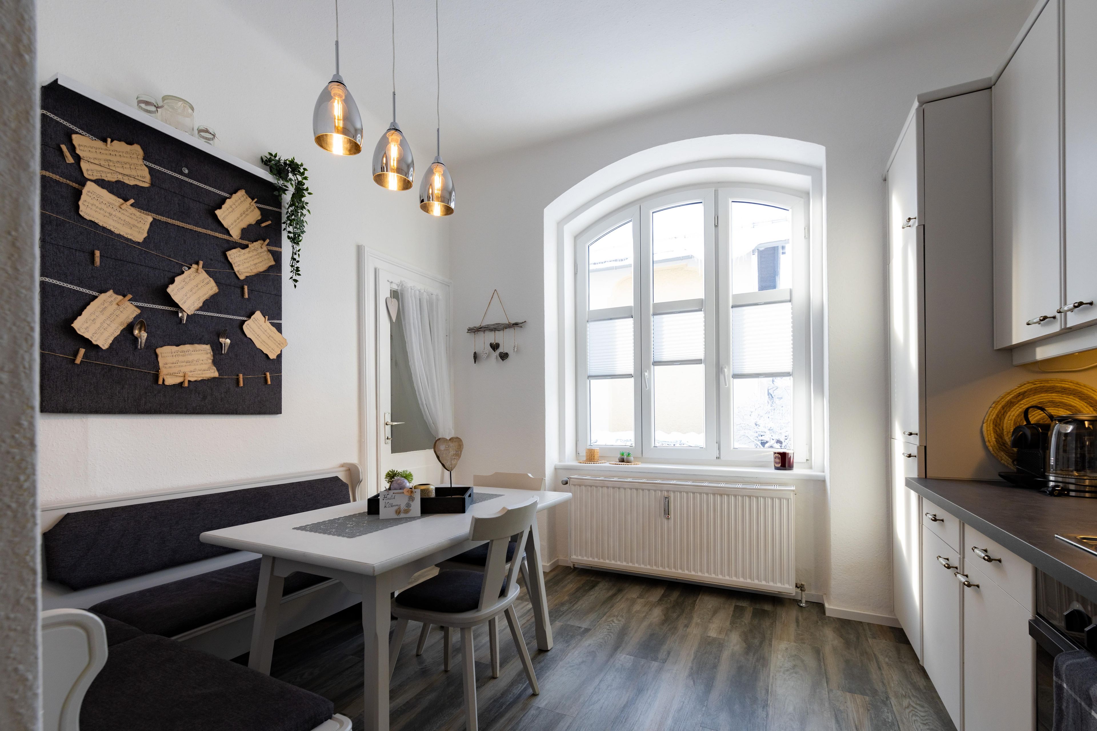 A modern kitchen with a dining area, white cabinetry, a large window, and a black and white wall art piece.