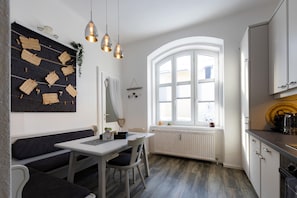 A modern kitchen with a dining area, white cabinetry, a large window, and a black and white wall art piece. - Mohr am Semmering (Semmering)