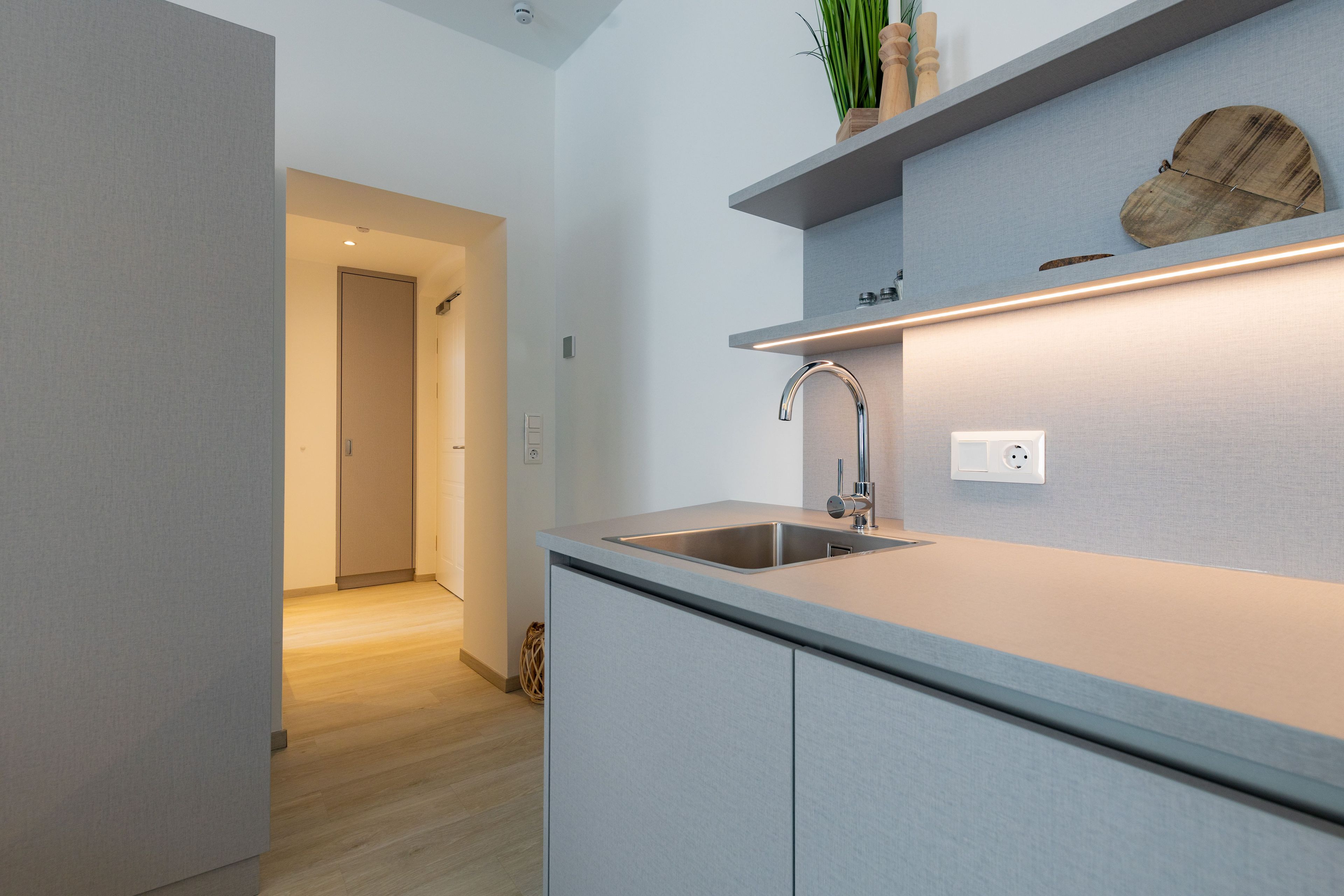 A modern kitchen with a stainless steel sink, a wooden shelf with decorative items, and a recessed ceiling light.