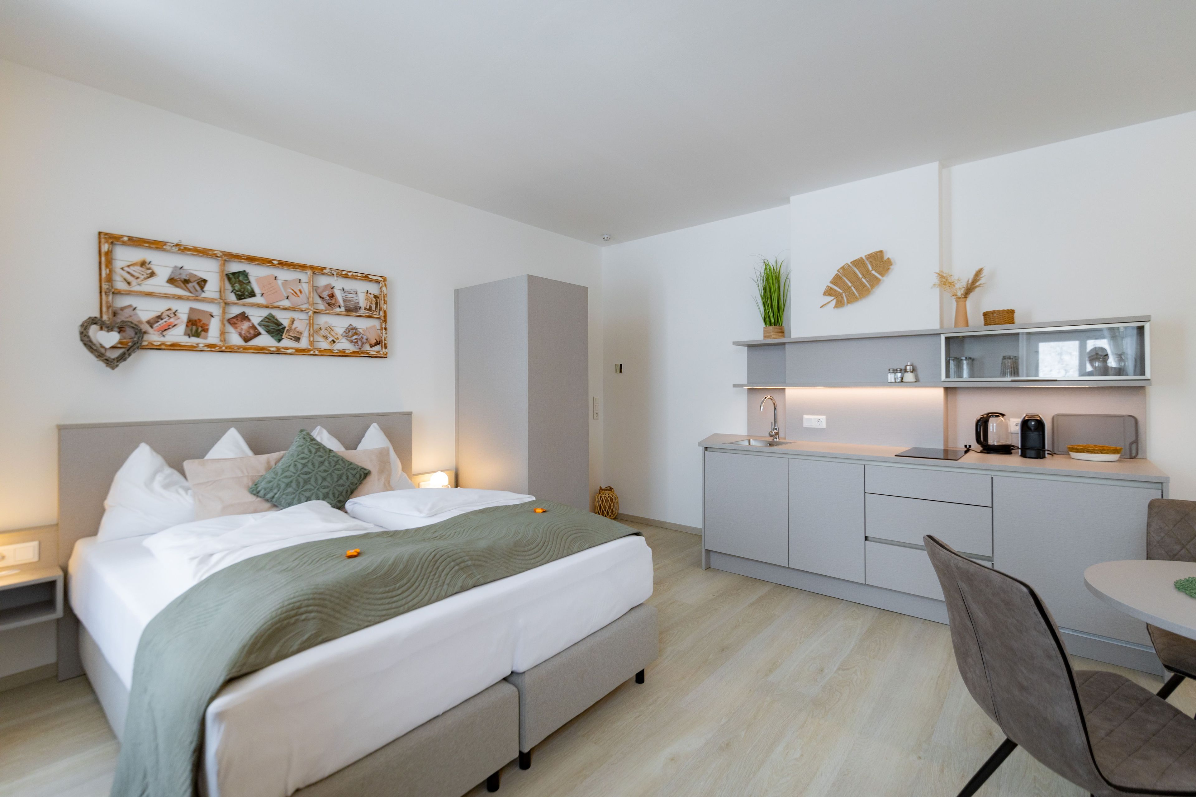 A modern hotel room with a bed, bedside table, and a small kitchenette.