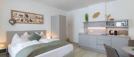 A modern hotel room with a bed, bedside table, and a small kitchenette.