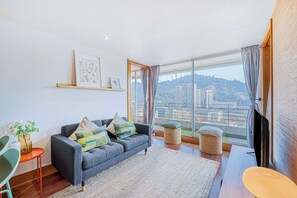 Uma sala de estar moderna com um sofá cinzento, uma mesinha e uma janela ampla com vista para a cidade.