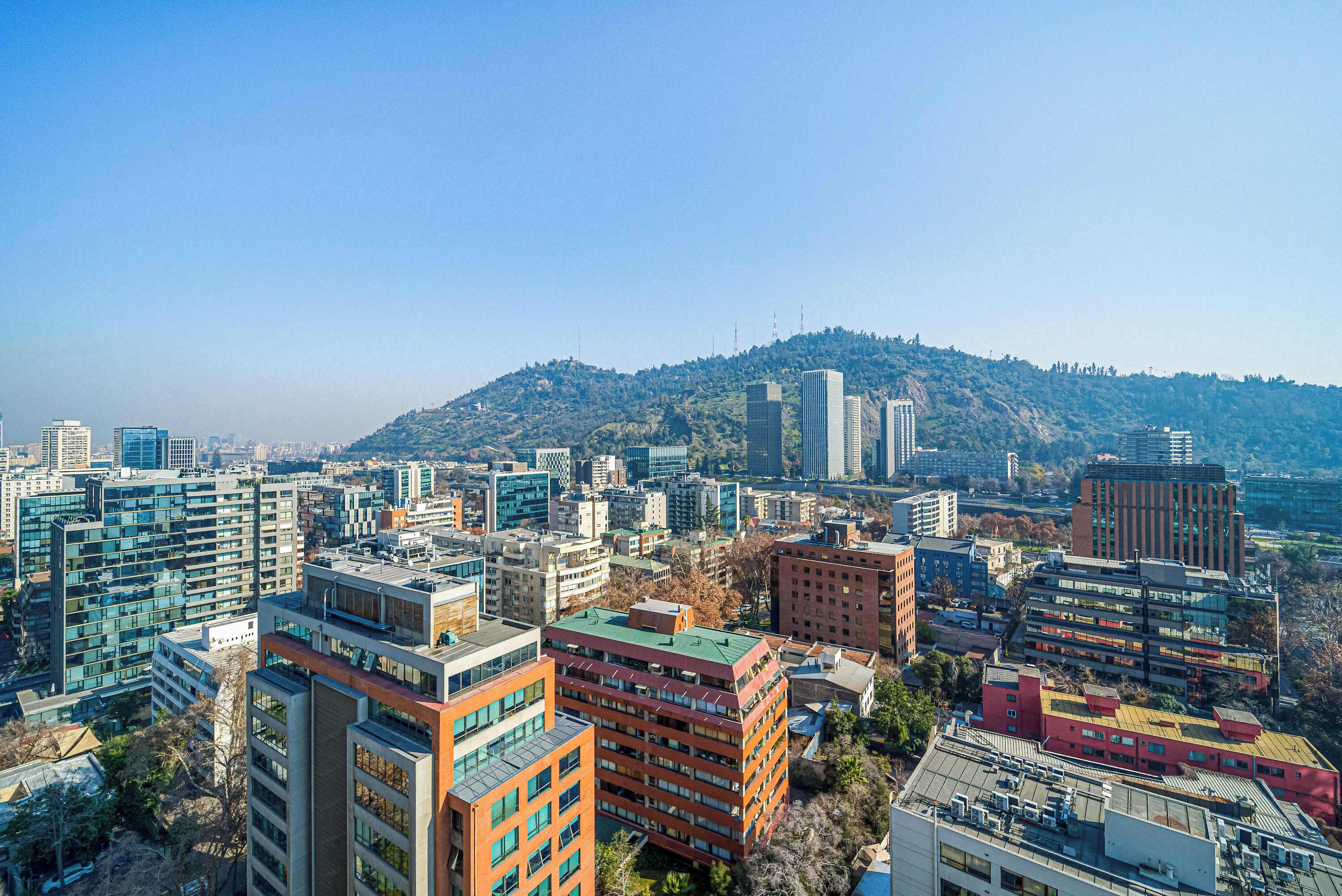 A cityscape with modern buildings, a hill in the background, and clear skies.