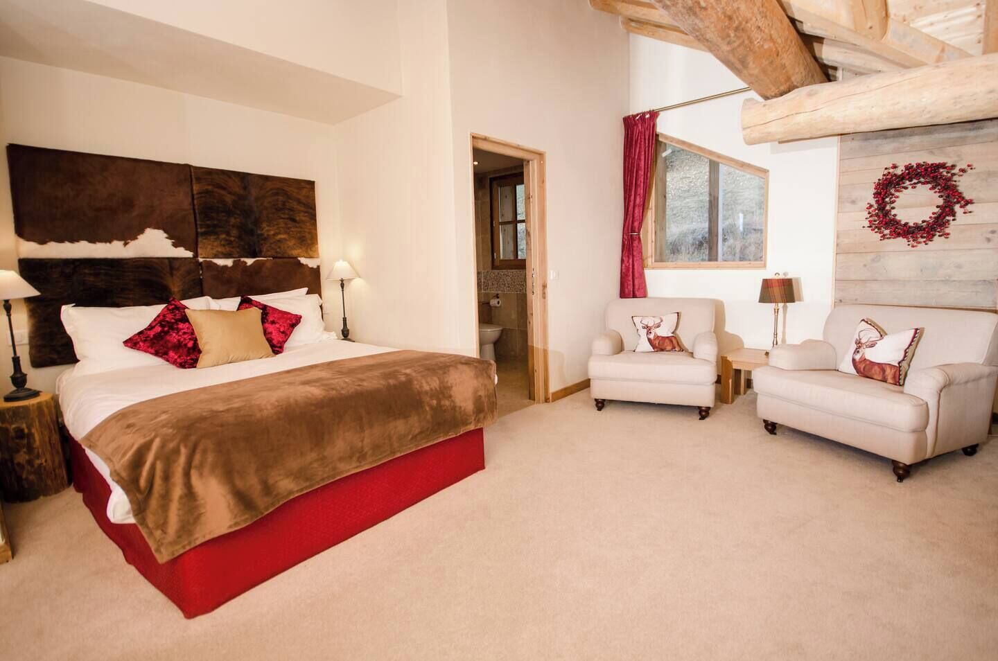 A bedroom with a large bed, two armchairs, a wooden headboard, and a red curtain.