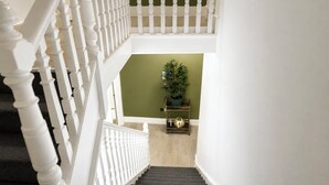 A staircase with white balusters, a green wall, and a small table with a potted plant. - KW SELF CONTAIN STUDIOS ALEXANDRA PALACE (London)